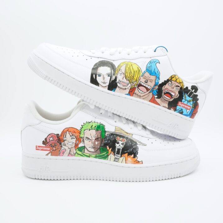 Weißer Nike Air Force 1 Sneaker mit handgemalten One Piece Charakteren wie Zorro, Sanji, Nami und weiteren Strohhutpiraten in bunten Anime-Designs auf den Seitenflächen.