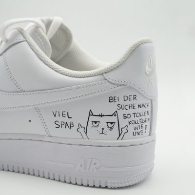 Weiße Nike Air Force 1 Sneakers mit einer Zeichnung und Text auf der Ferse.