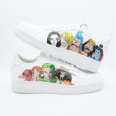Weißer Nike Air Force 1 Sneaker mit handgemalten One Piece Charakteren wie Zorro, Sanji, Nami und weiteren Strohhutpiraten in bunten Anime-Designs auf den Seitenflächen.