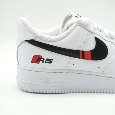 Weißer Nike Air Force 1 Sneaker mit schwarzem Swoosh und rotem Streifen auf der Seite.