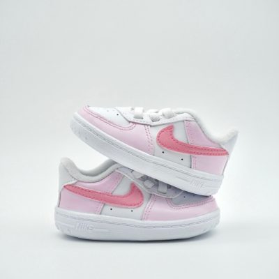 Zwei kleine Babysneaker im hellen Rosa-Weiß mit dunklerem rosa Swoosh und kleinen rosa Akzenten an Sohle und Mittelfeld auf hellem Hintergrund.