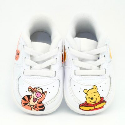 Paar weiße Baby-Sneaker mit handgemaltem Winnie-Puuh-Design, Tigger-Motiv auf einem Schuh und Pu-der-Bär-Motiv auf dem anderen Schuh