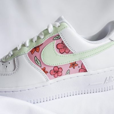Weiße Nike Air Force 1 Sneakers mit floralem Design in Pink und Grün auf der Seite.