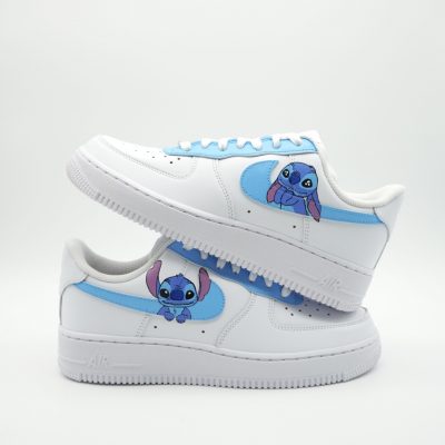 Weiße Sneaker mit hellblauen Akzenten und einer Cartoon-Illustration von Stitch aus Disneys Lilo & Stitch an den Seitenteilen. Vor einem schlichten weißen Hintergrund liegt ein Schuh über dem anderen.