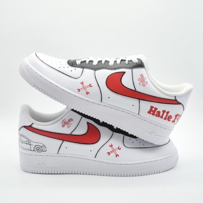 Zwei weiße Sneaker mit roten Nike-Swooshs, schwarzen Details und einzigartigen handgezeichneten Grafiken, darunter Schneeflocken, ein Auto und die Worte „Halle 13“. Die Schuhe sind gestapelt, wobei ein Schuh auf dem anderen liegt.
