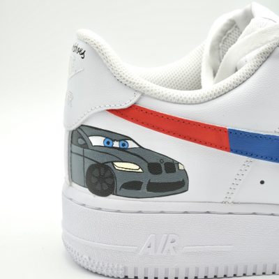 Weißer Sneaker mit einem individuellen Cartoon-Autodesign in Grau und Blau auf der Ferse und roten und blauen Streifen an der Seite auf schlichtem weißem Hintergrund.
