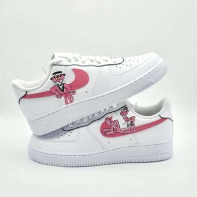 Zwei weiße Sneaker mit Pinken Nike-Swooshs und handgezeichneten Grafiken, die den rosa roten Panther zeigen. Die Schuhe sind gestapelt, wobei ein Schuh auf dem anderen liegt.