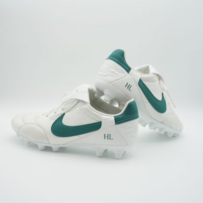Weiße Fußballschuhe mit grünen Details und dazu passenden Initialen.