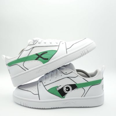 Weißer Puma Sneaker für Fotograf mit grünem Swoosh, gemalter schwarz-grüner Kamera und feinen schwarzen Konturlinien auf den Seiten in puristischem Design.