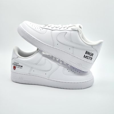 Weißer Nike Air Force 1 mit dezent gemaltem Wappen der Stadt Steinheim, weißem Swoosh mit Tropfen-Effekt und schwarzer Aufschrift 'BRGR MSTR' für Bürgermeister an der Ferse.