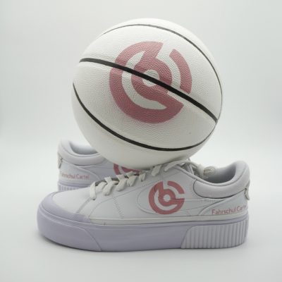 Weißer Nike Sneaker mit rosa Fahrschule-Cartel Logo auf dem Swoosh und der Ferse, balanciert auf einem weißen Basketball mit identischem rosa Markenlogo im Studio.