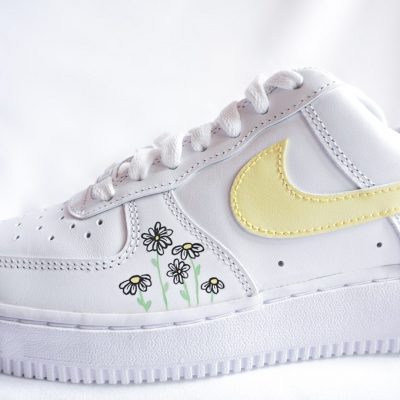 Weiße Sneakers mit gelbem Nike-Swoosh und Blumenmuster auf der Seite.
