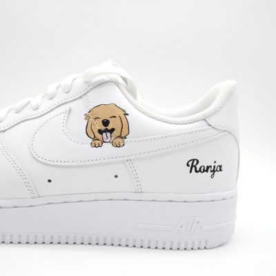 Nahaufnahme eines weißen Nike Air Force 1 mit gemaltem Golden Retriever Welpen Porträt auf dem Swoosh und schwarzem 'Ronja' Schriftzug an der Ferse.