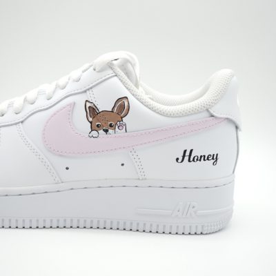 Nahaufnahme eines weißen Nike Air Force 1 mit rosa Swoosh, kleinem Chihuahua-Welpen Porträt und schwarzer 'Honey' Schreibschrift an der Ferse.