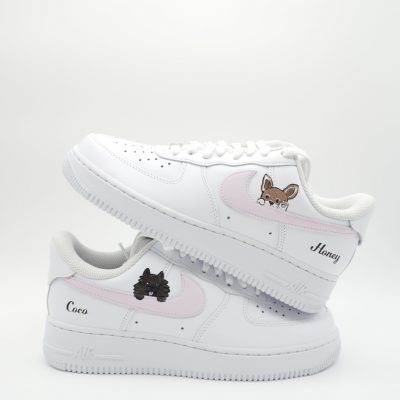 Zwei gestapelte weiße Nike Air Force 1 Sneaker mit rosa Swoosh, gemalten Hunde-Porträts und personalisierten Namen 'Honey' und 'Coco' an den Fersen.