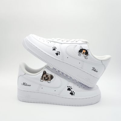 Zwei gestapelte weiße Nike Air Force 1 mit kleinen Hunde- und Katzen-Porträts, gestreuten schwarzen Pfotenabdrücken und personalisierten Namen 'Milow' und 'Pikie'.