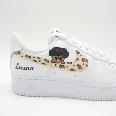Nahaufnahme eines weißen Nike Air Force 1 mit Leoparden-Swoosh, gemaltem Rottweiler-Welpen Porträt und 'Luana' Schriftzug in schwarzer Schreibschrift an der Ferse.