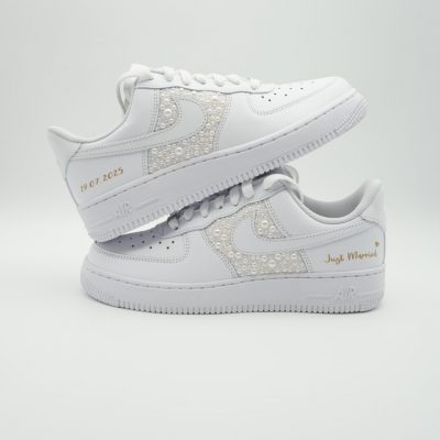 Zwei gestapelte weiße Nike Air Force 1 mit perlenbesetztem Swoosh, goldenem Schriftzug 'Just Married' und goldenem Datum '18.07.2025' an den Fersen.