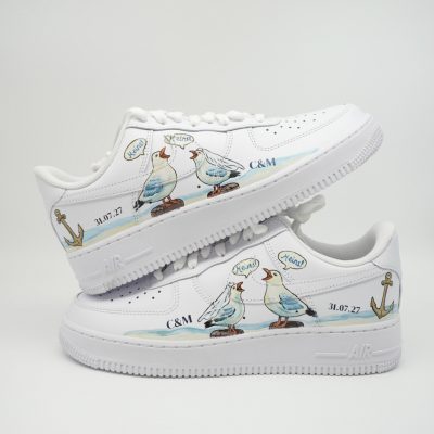 Zwei gestapelte weiße Nike Air Force 1 Hochzeitssneaker mit handgemalten Möwen-Paaren, Sprechblasen 'Meins!', Ankern, Initialen 'C&M' und Datum '31.07.27'.