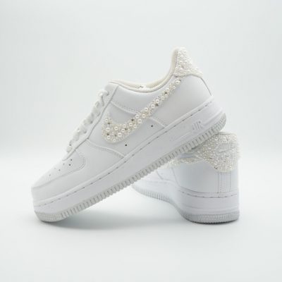 Zwei weiße Nike Air Force 1 mit dicht perlenbesetztem Swoosh in dezenten weiß-cremefarbenen Perlen ohne weitere Aufschriften im schlichten Hochzeitsdesign.