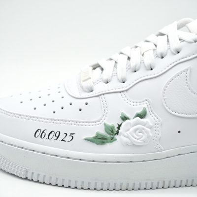 Detailaufnahme eines weißen Nike Air Force 1 mit aufgesetzter weißer 3D-Rose, grünem Blatt und silberner Datumsangabe '06.09.25' auf der Sohlenseite.