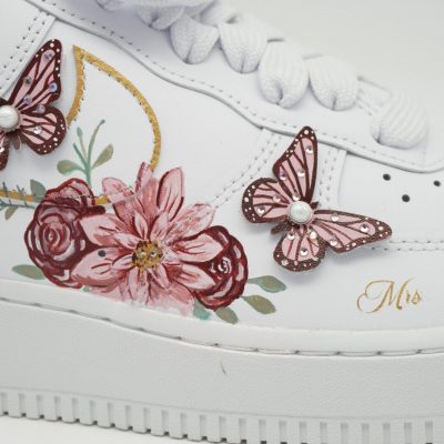 Nahaufnahme eines weißen Nike Air Force 1 mit handgemalten Rosen, rosa Blüten und zwei aufgesetzten 3D-Schmetterlingen mit Perlen sowie goldenem 'Mrs' Schriftzug.