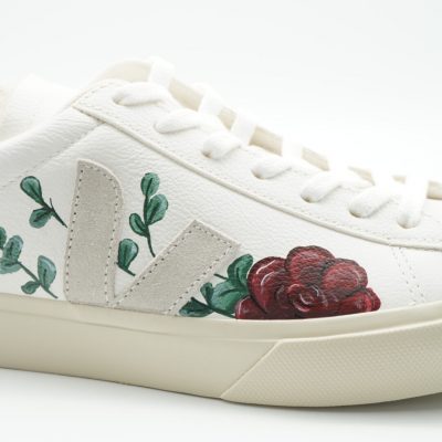 Nahaufnahme eines weißen Veja Sneakers mit handgemalter roter Rose, grünen Eukalyptus-Zweigen entlang der Seite und feinen Konturen im naturnahen Hochzeitsdesign.