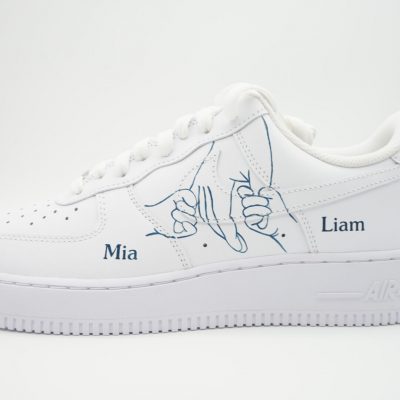 Weißer Nike Air Force 1 mit handgemaltem 'Pinky Promise' Motiv aus zwei verhakten kleinen Fingern in Blau und blauen Namen 'Mia' und 'Liam' auf den Seitenflächen.