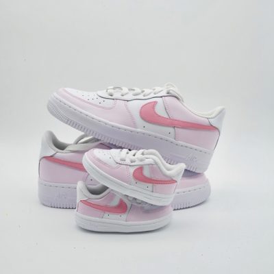 Großer und kleiner weißer Nike Air Force 1 Sneaker mit rosa Swoosh und rosa Stoffeinsätzen, Mama-und-Baby-Set vor weißem Hintergrund.
