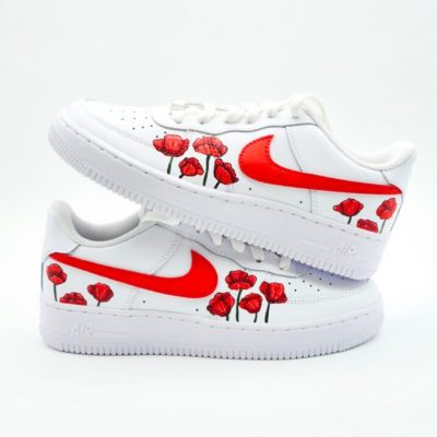 Weißer Nike Air Force 1 Sneaker mit handbemalten roten Mohnblumen entlang der Seiten und kräftig rot lackiertem Nike-Swoosh auf hellem Studiohintergrund.