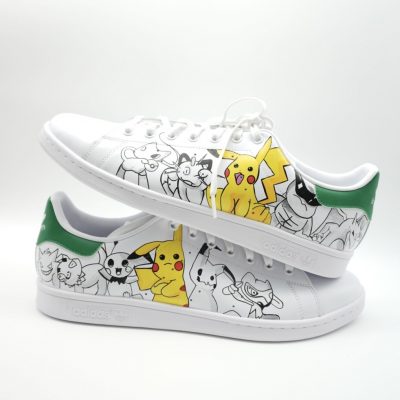 Weiße Adidas Stan Smith Sneakers mit Pokémon-Motiven, einschließlich Pikachu, auf der Seite.