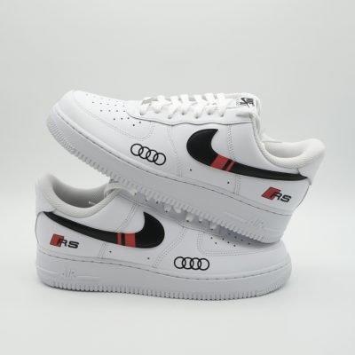 Zwei gestapelte weiße Nike Air Force 1 mit schwarzem Swoosh, rot-schwarzem Streifen, Audi-Ringen und 'RS' Schriftzug an der Ferse im sportlichen Audi-Design.