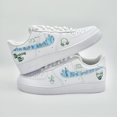 Zwei gestapelte weiße Nike Air Force 1 im Breaking Bad Design mit hellblauen Kristallen, grünen Pflanzen, schwarzem Logo und 'Let's Cook' Schriftzug an der Seite.