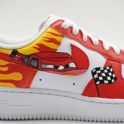 Roter Nike Air Force 1 Custom Sneaker mit Lightning McQueen Motiv aus Cars, Flammen und Zielflagge auf dem Mittelfußbereich, seitliche Nahaufnahme vor hellem Hintergrund