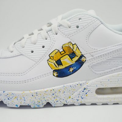 Weißer Nike Air Max Custom Sneaker mit Clash Royale Burg-Motiv in Gelb und Blau auf dem Mittelfußbereich, blau-gelbe Farbspritzer auf der Sohle, seitliche Nahaufnahme