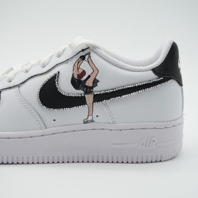 Weißer Nike Air Force 1 Custom Sneaker mit Eiskunstlauf-Motiv, Eiskunstläuferin in Pose auf schwarzem Swoosh und Glitzersteinen am Mittelfußbereich