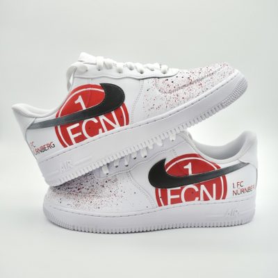 Paar weiße Nike Air Force 1 Custom Sneaker mit 1 FC Nürnberg Logo, schwarzer Swoosh rotes FCN-Vereinswappen und rote Farbspritzer auf den Außenseiten