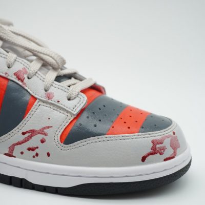 Custom Sneaker mit Freddy Krueger Design, rot-grau-gestreiftes Muster mit Blutspritzer-Effekt, Nahaufnahme der Außenseite mit Schnürsenkeln vor hellem Hintergrund