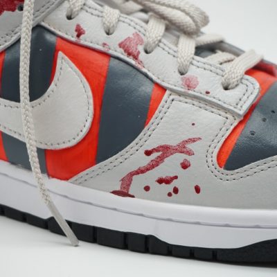 Custom Sneaker mit Freddy Krueger Design, rot-graue Streifen mit weißem Swoosh und Blutspritzer-Motiven, seitliche Nahaufnahme der Außenseite vor neutralem Hintergrund
