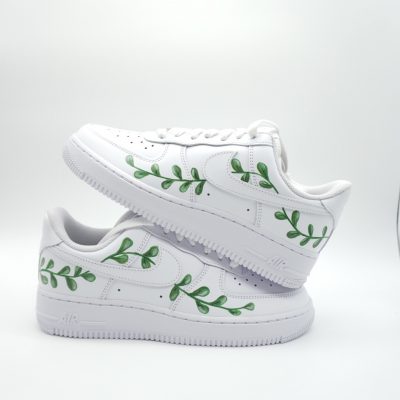 Zwei gestapelte weiße Nike Air Force 1 mit kreisförmig angeordneten grünen Blätter-Ranken um den Swoosh als Kommunion-Design im schlichten Look.