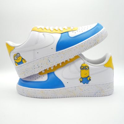 Zwei gestapelte weiße Nike Air Force 1 mit handgemalten Minion-Motiven, blau-gelb gefärbten Mittelfeldern und farbenfrohen Punkten auf den Sohlen.