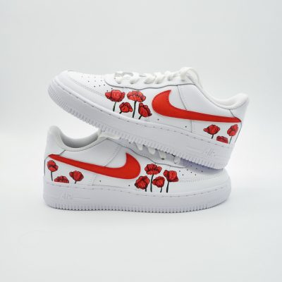 Zwei gestapelte weiße Nike Air Force 1 mit rotem Swoosh und handgemalten roten Mohnblumen entlang der Sohle, dynamisch nach oben wachsend an beiden Seiten.