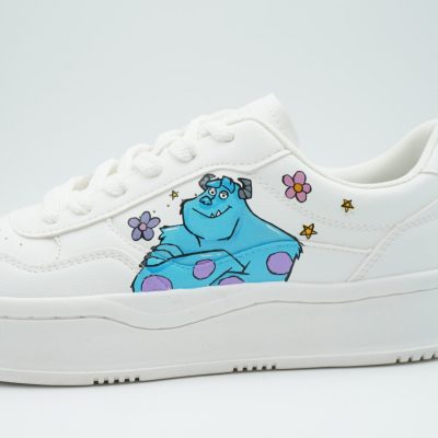 Nahaufnahme eines weißen Plateau-Sneakers mit handgemaltem Sulley aus Monster AG, kleinen lila Blumen und gelben Sternchen als verspieltes Filmdetail.