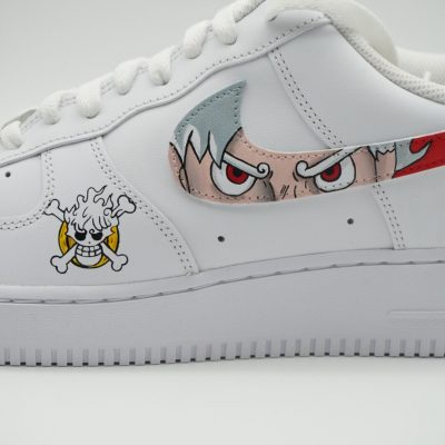 Weißer Nike Air Force 1 Custom Sneaker mit One Piece Motiv, Augen einer Figur auf dem Swoosh und Strohhut-Totenkopf-Logo, seitliche Nahaufnahme vor neutralem Hintergrund