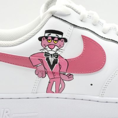 Nahaufnahme eines weißen Nike Air Force 1 mit handgemaltem Pink Panther im Smoking, rosa Swoosh und feiner Comic-Illustration als verspieltes Retro-Detail an der Seite.