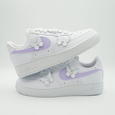 Paar weiße Nike Air Force 1 Custom Sneaker mit hellvioletten Schmetterling-Motiven auf dem Swoosh, 3D-Schmetterlinge auf der Zunge und am Mittelfußbereich, gestapelte Präsentation