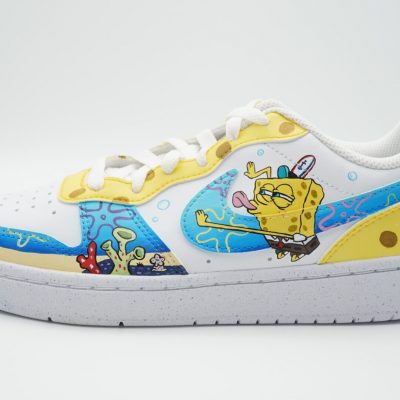 Weißer Custom Sneaker mit SpongeBob-Design auf gelbem Swoosh und Unterwasserwelt-Motiven, seitliche Detailansicht vor hellgrauem Hintergrund mit Korallen und Wasserblasen