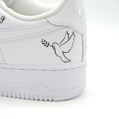 Nahaufnahme eines weißen Nike Air Force 1 mit handgemalter Friedenstaube mit Olivenzweig im Schnabel als zartes Tauf-Motiv an der Ferse.
