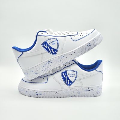 Paar weiße Nike Air Force 1 Custom Sneaker mit VfL Bochum Design, blaues Vereinslogo mit Schriftzug Bochum 1848 und blaue Farbspritzer auf den Außenseiten