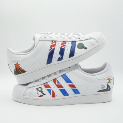 Paar weiße Adidas Superstar Custom Sneaker mit Reise-Design, Island-Flagge in Streifen Vulkan Papageientaucher und Pinguin-Motive auf den Seiten